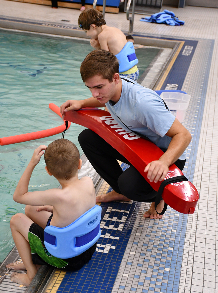 A lifeguard at a pool talking to a young child. 