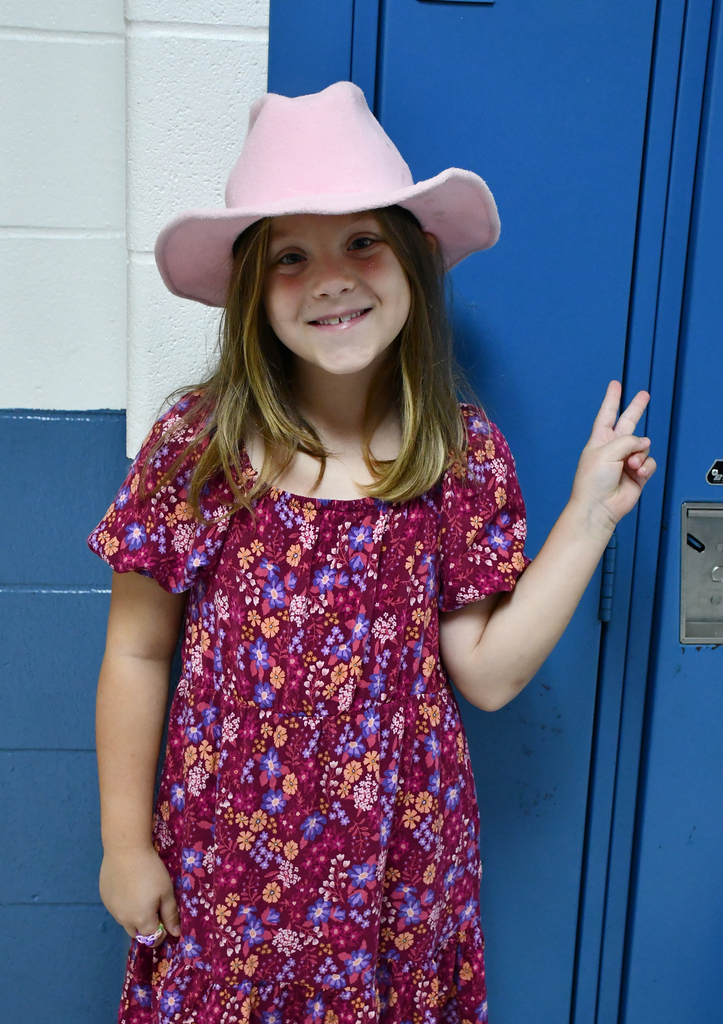 A girl in a pink hat, holding up a 'Peace' sign. 