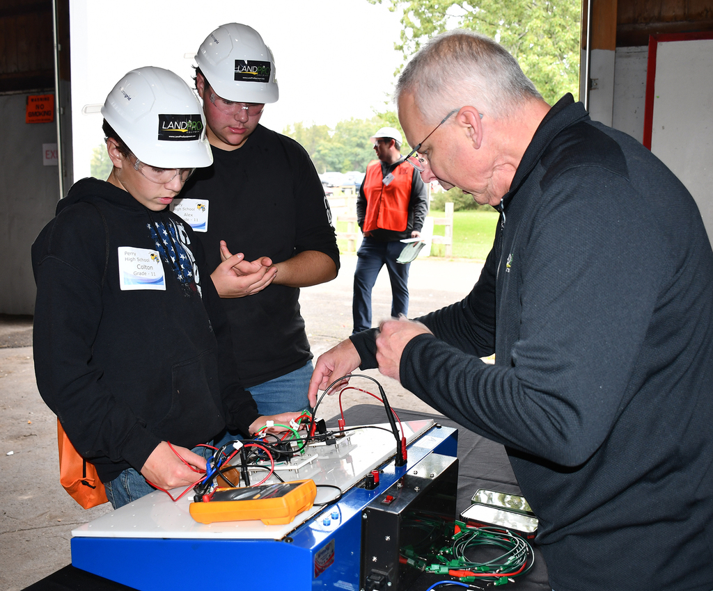 An adult helping two students with electronics. 