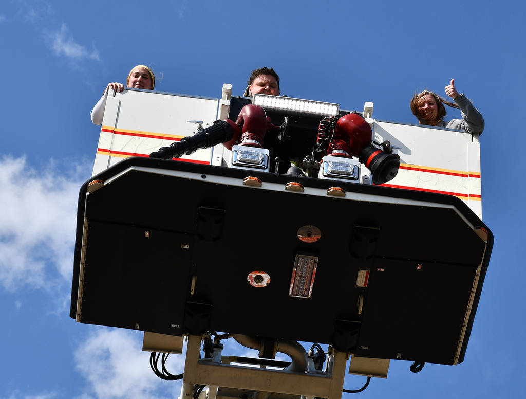 Three adults in a fire truck lift. 