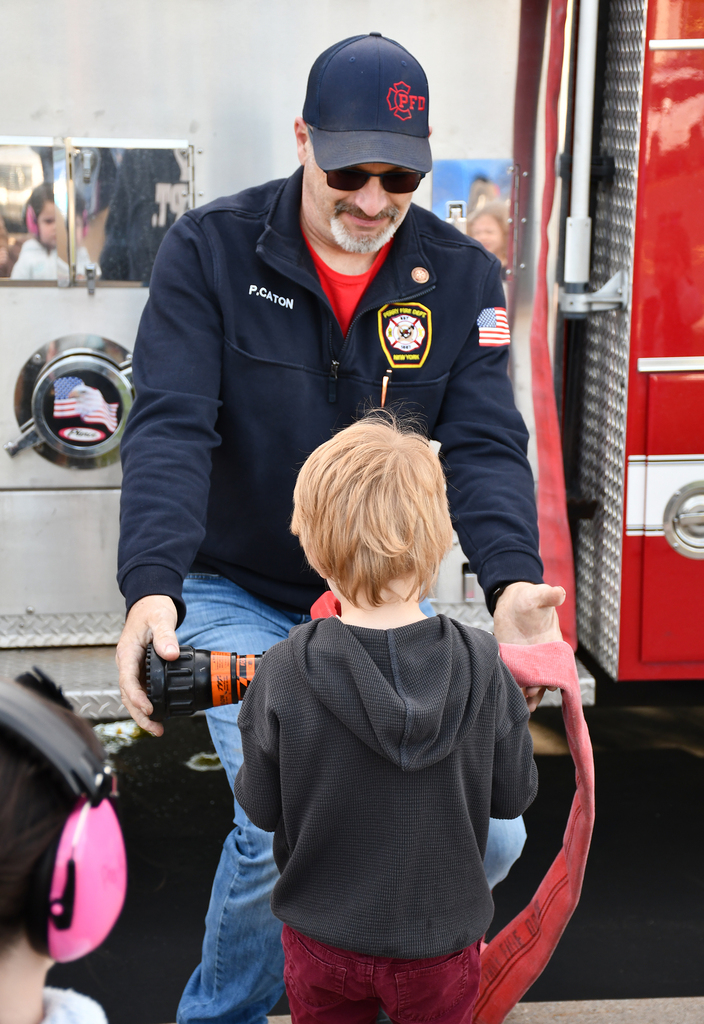 A fireman showing a boy a fire hose off of a fire truck. 