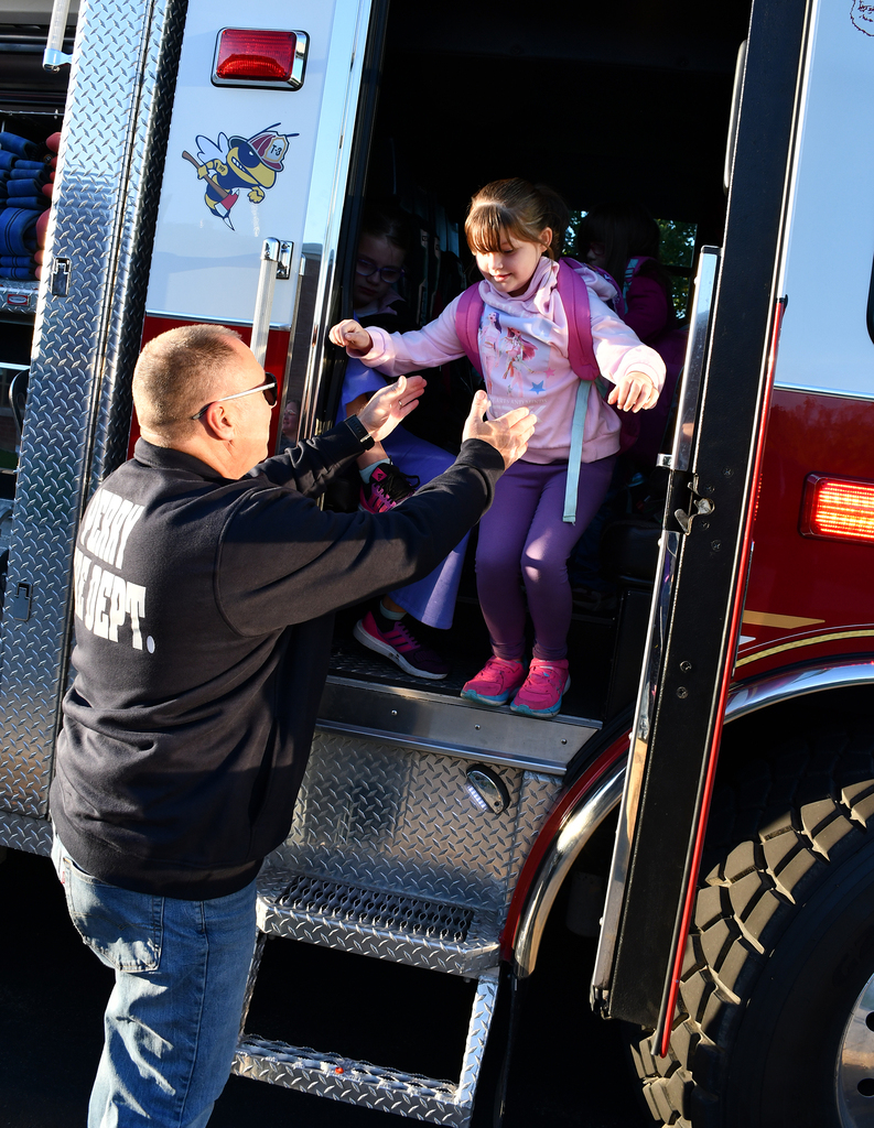 A fireman helping a little girl out of a fire truck. 