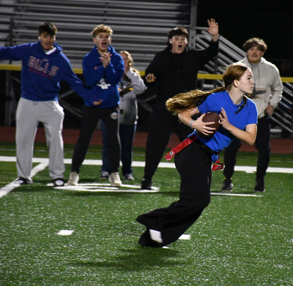 A girl running with a football while others cheer in the background. 