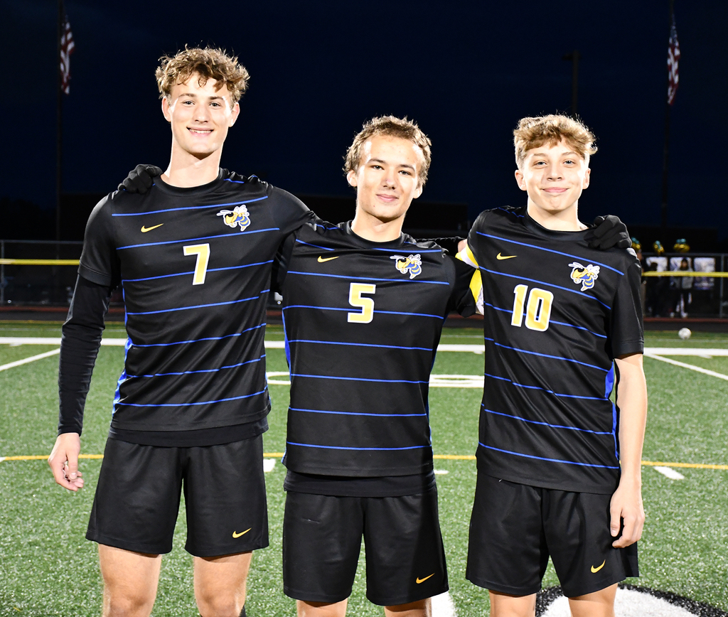 Three boys standing on a soccer field. 