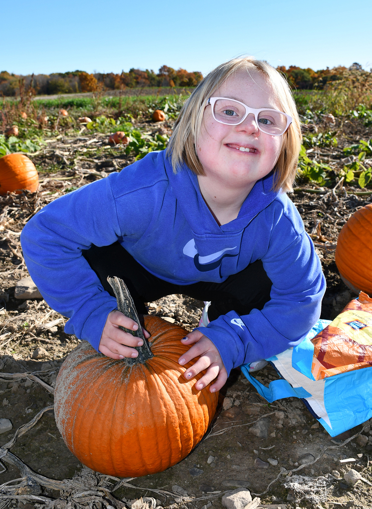 A student kneeling by a pumpkin in a pumpkin patch. 