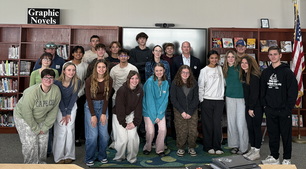 A high school class posing with a male adult in a school library.