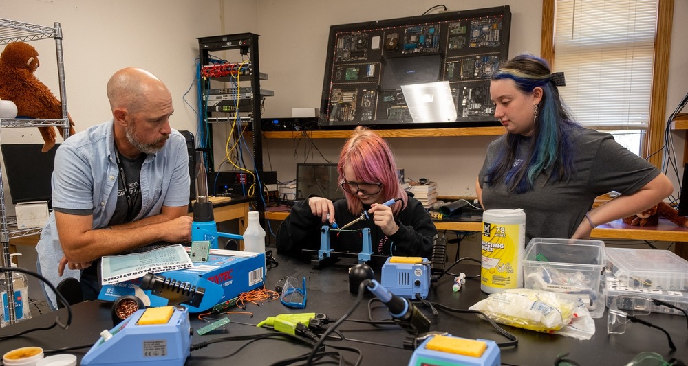 A student solders an electronics project as an instructor supervises.