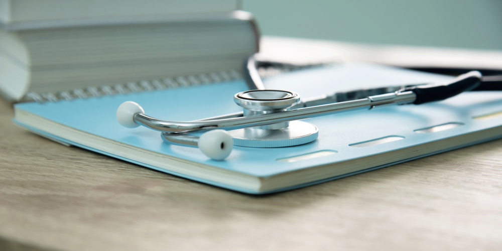 A stethoscope lying on a notebook on a desk.