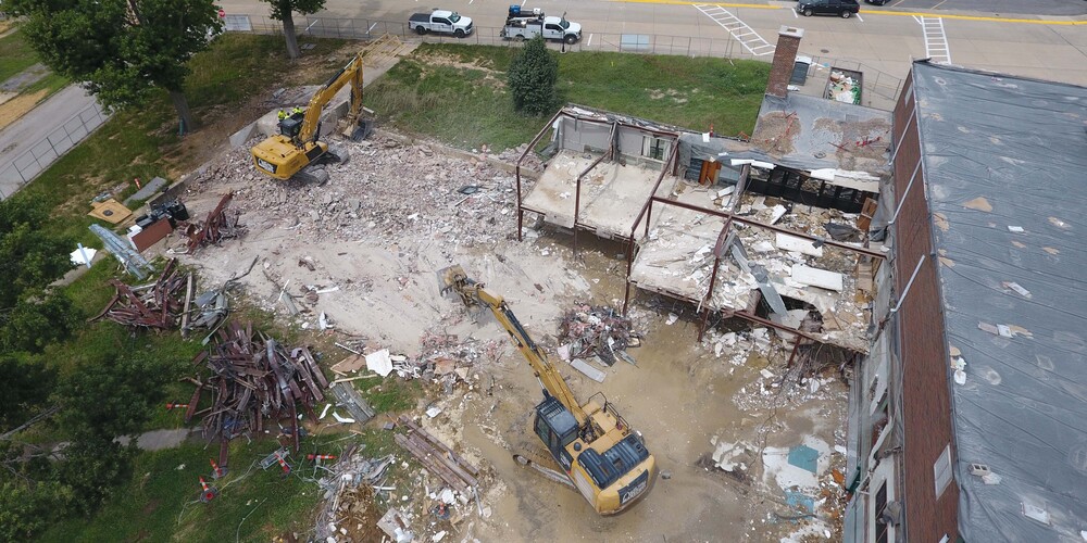 Two yellow excavators work to clear debris at a building demolition site.