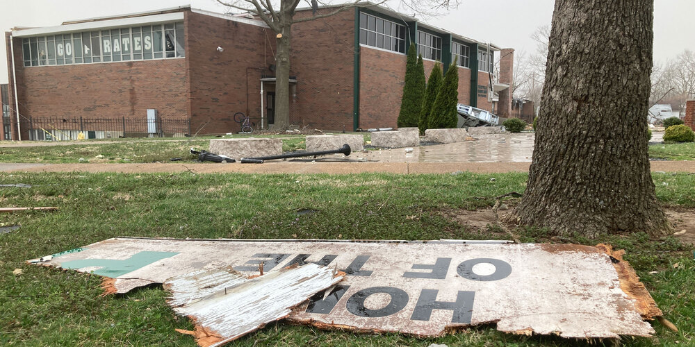 The damaged PHS building is in the background. In the foreground are broken pieces of a sign that says "home of the pirates"