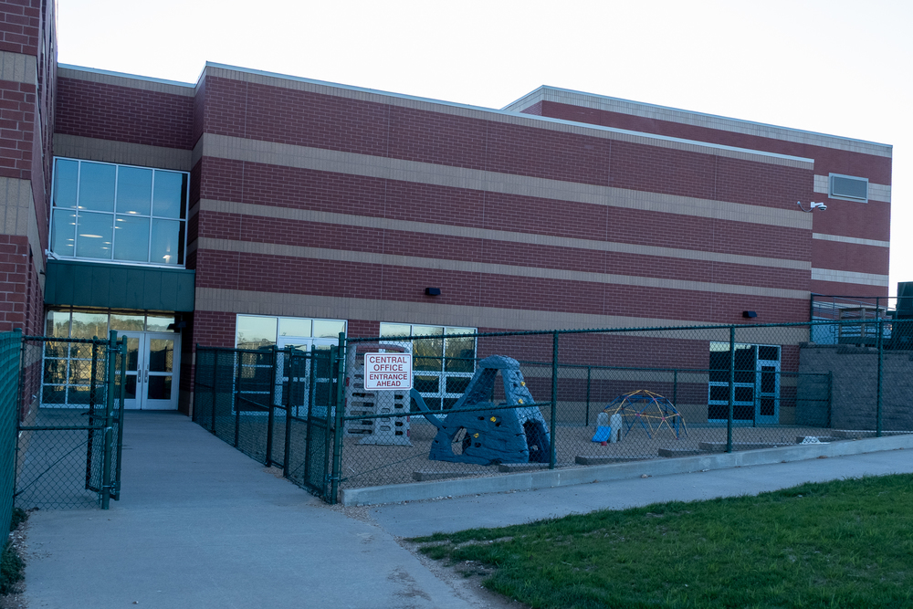 A view of the new Central Office at the rear of the Perryville Primary Center. There is green chan link fencing with an open gate leading to doors at the back of the building. To the right is a small playground surrounded by the fencing.