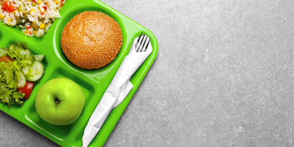 Image of a green lunch tray with an apple, a sesame seed bun, a salad, and a vegetable rice mix.