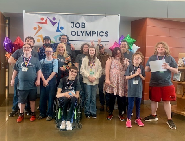 PHS SPED students stand in front of a "Job Olympics" banner. Several of the students have medals around their necks.