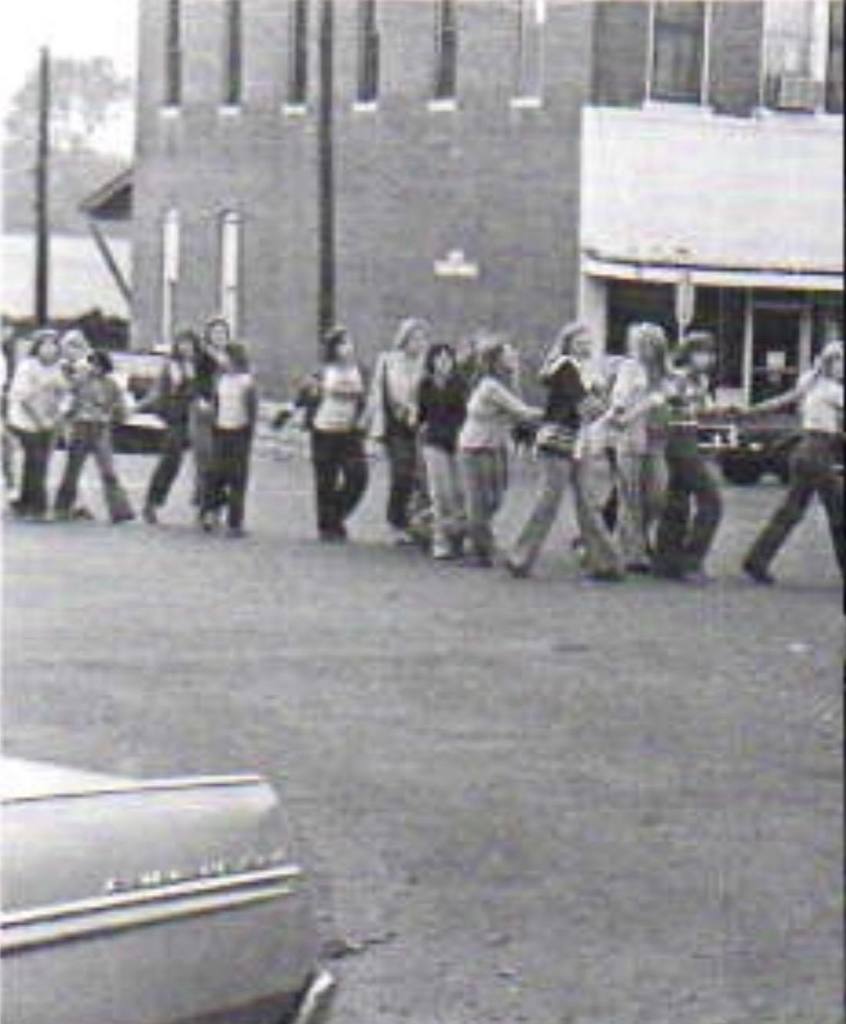 An old black and white yearbook photo of students joining hands and walking through the Perryville town square in a Snake Dance from the past.