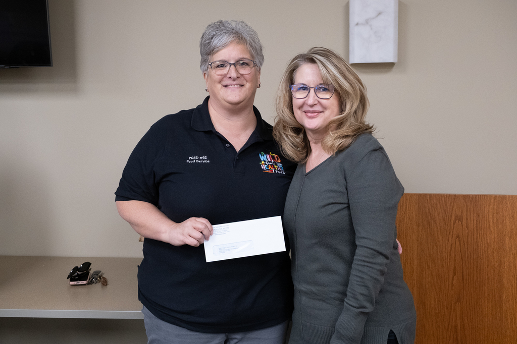 District 32 Director of Food Serivces Debbie Baer is pictured alongside AMM staff member Cheryl Winschel. Baer is holding an envelope with a donation presented by Winschel on behalf of AMM employees.
