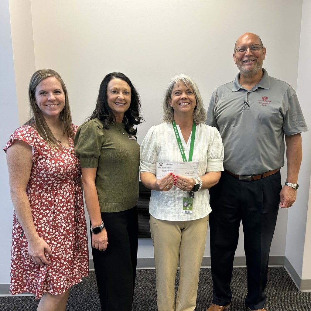 Four individuals pose for a photo. One person is holding a donated check.