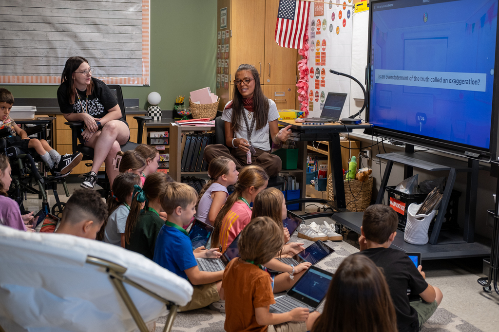 A teacher speaks to her class seated on the rug in front of her.