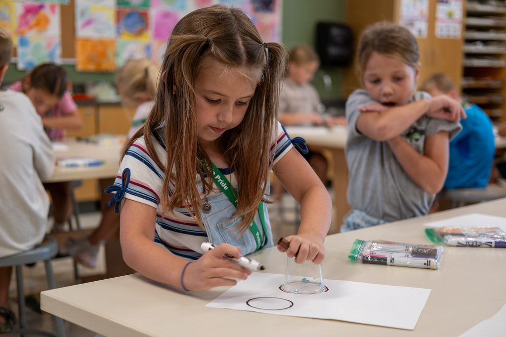 A student traces circles using a plastic cup