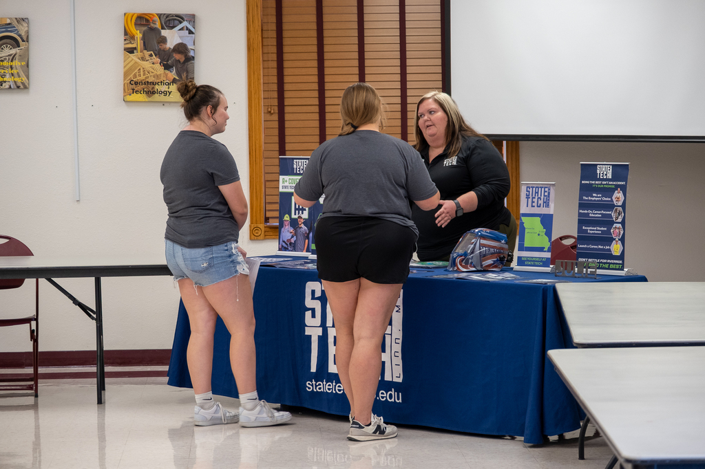 Students interact with an individual at a table during a career/college fair.