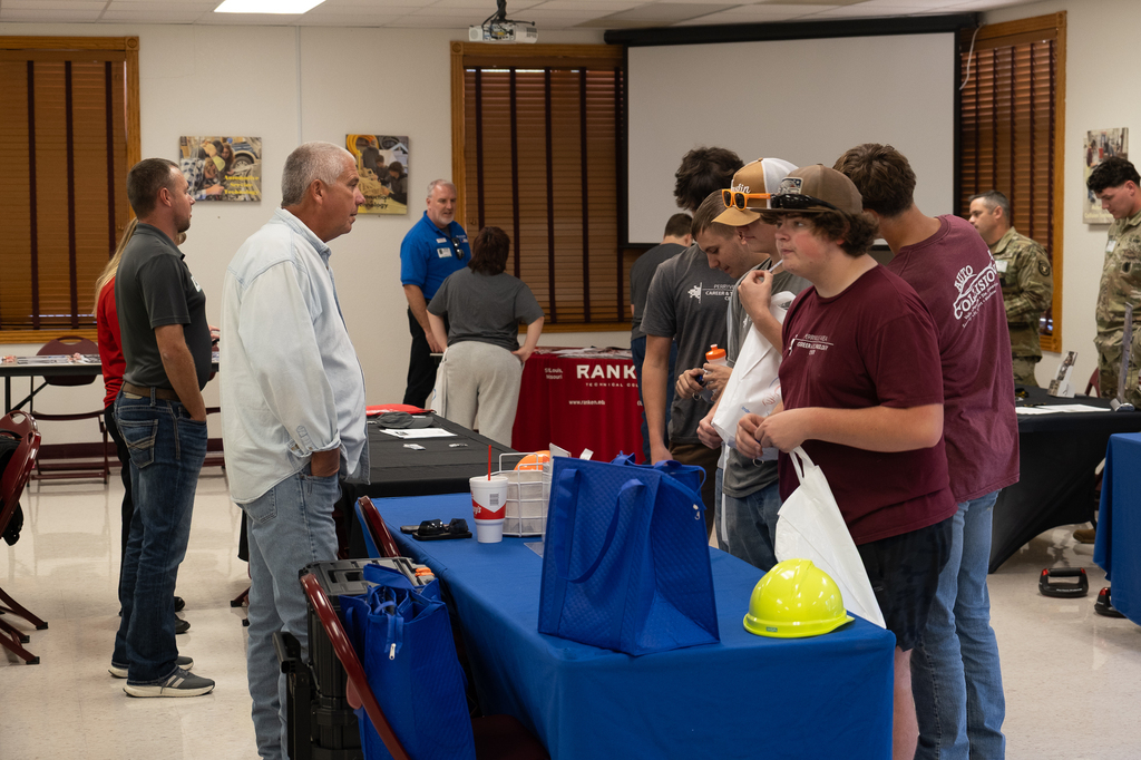 Students interact with an individual at a table during a career/college fair.