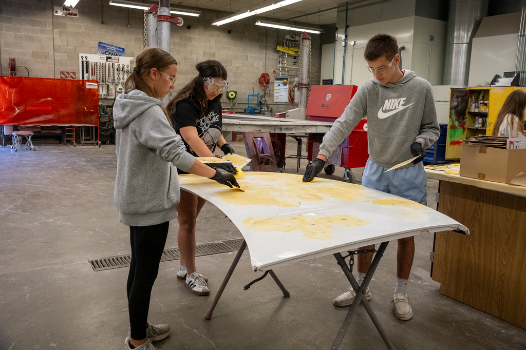 Three students apply body filler to a car hood.