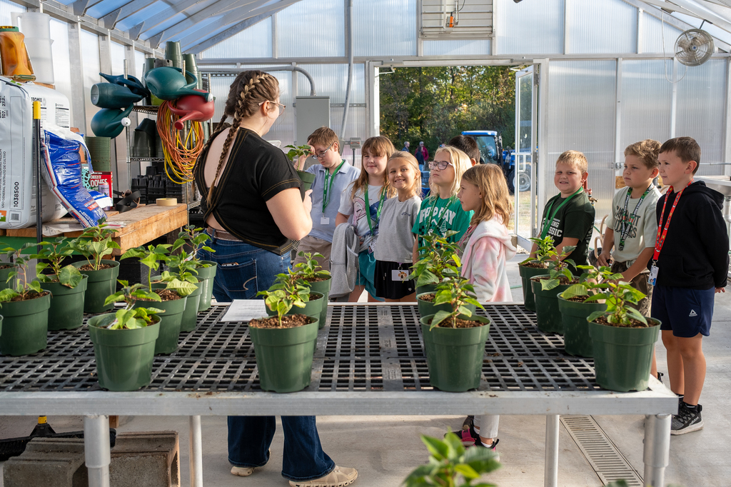 An older student teaches younger students about plants in a greenhouse.