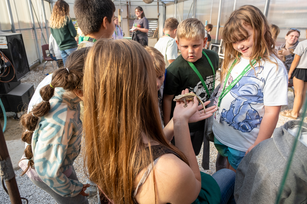 An older student holds a gecko for younger students to see.