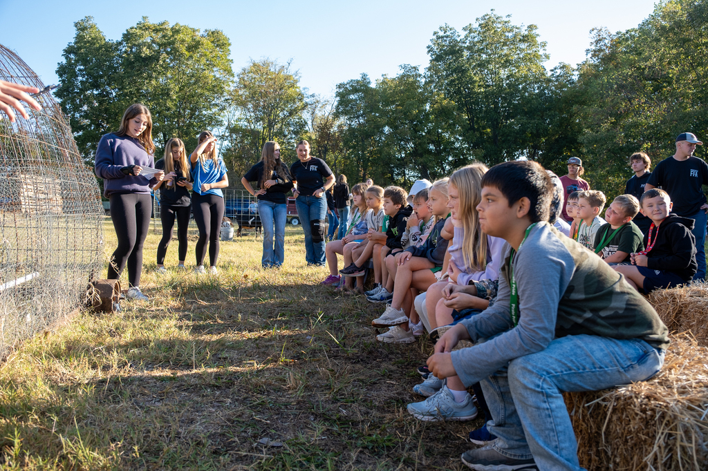 Elementary students sit on a hay bale and listen to a presentation.