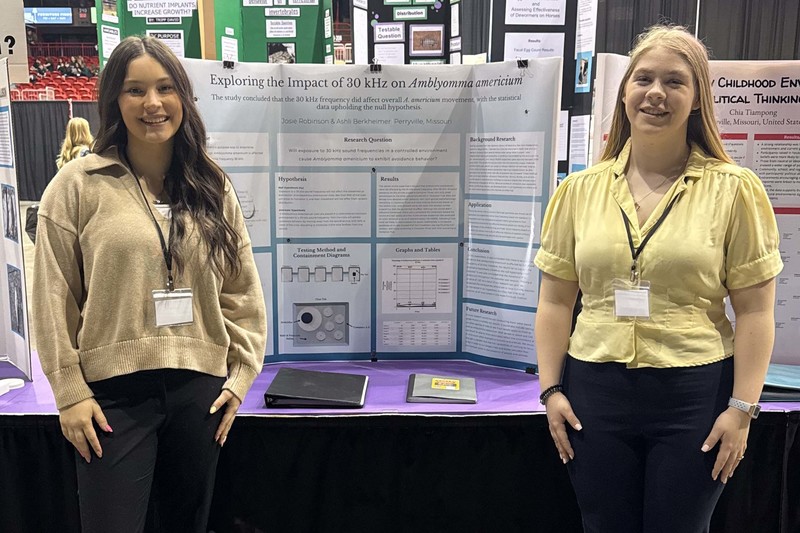 Ashli Berkheimer and Josie Robinson stand next to their science fair project.