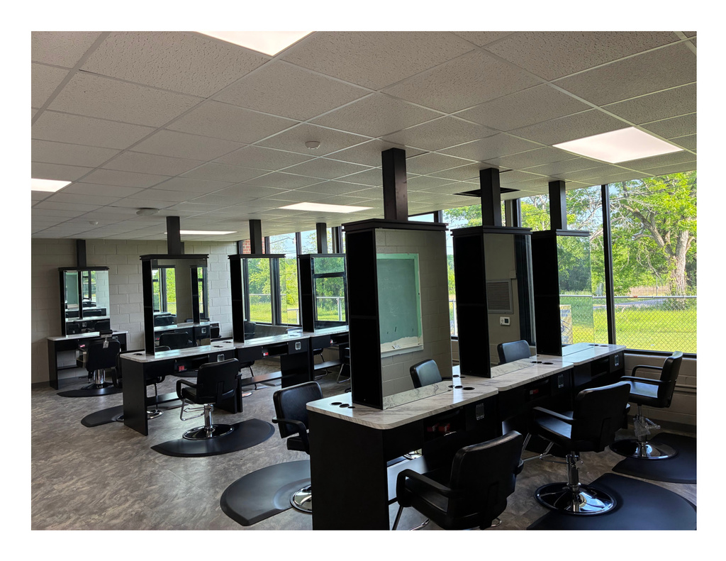 Modern cosmetology classroom featuring professional salon stations with mirrors, styling chairs, countertops, and large windows. The renovated training space at Robert C. Hatch High School is designed to provide students with hands-on cosmetology and career readiness experiences in a salon-style learning environment.