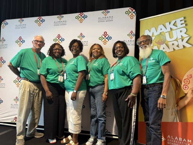 Six members of the Perry County Board of Education, including Superintendent Dr. Marcia Smiley, pose together at the 2026 Alabama Association of School Boards Summer Conference. The group is standing in front of an Alabama Association of School Boards backdrop and a banner displaying the conference theme, "Make Your Mark." All are wearing matching green shirts and conference name badges. The photo reflects the board's participation in professional learning and leadership development activities focused on strengthening public education and supporting student success.