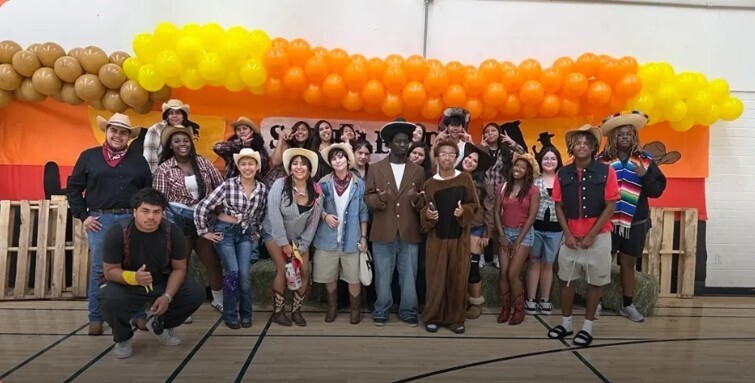 Group of kids wearing hats and orange, yellow and brown balloons in the background