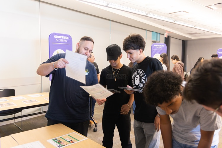 man shows 2 students some papers