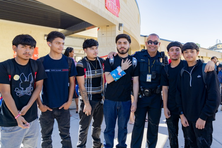 Group of students, including a police officer, stand in front of a building. Some wear bracelets.