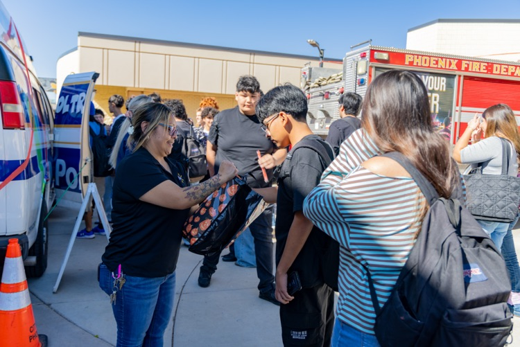 People gather outside with a fire truck in the background; some wear backpacks and hold onto each other.