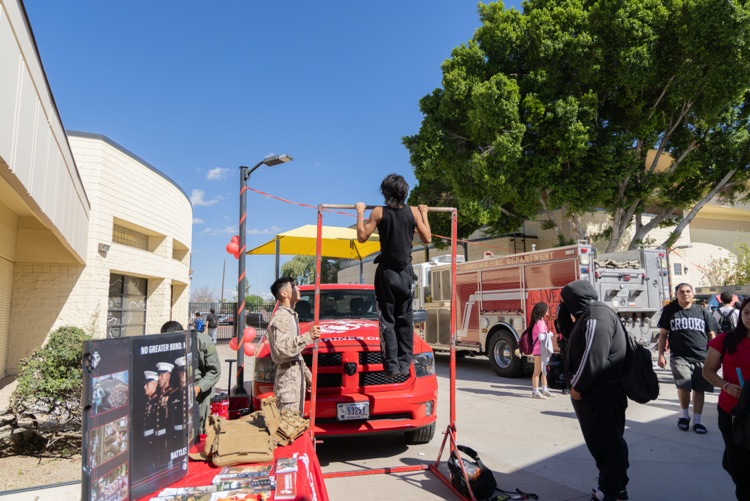 A person on a red platform outside a building, a red vehicle, a fire truck, people walking.