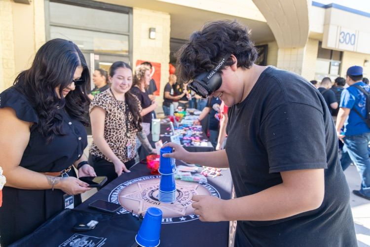 A group of people gather around a table with a game setup. A boy is playing a game using cups.