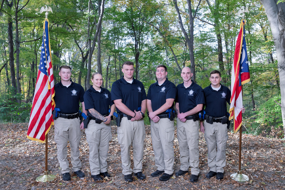 a group of students stand with 2 adults in front of a veterans history project banner. 