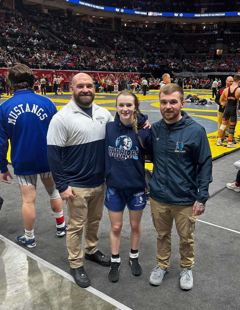 a female wrestler poses with two male coaches