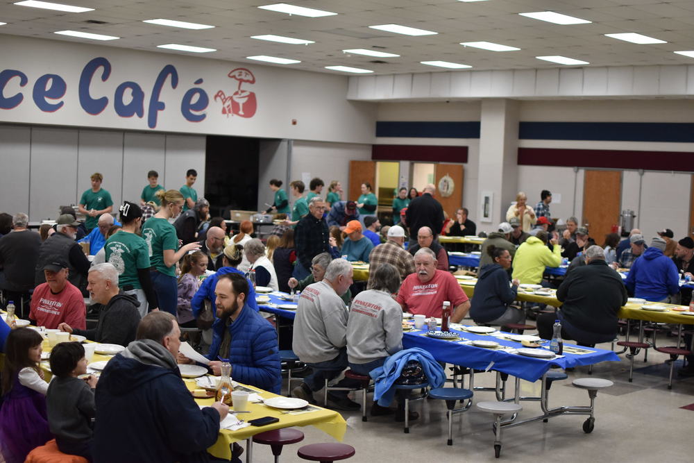 A cafeteria is full of people of all ages for a community breakfast. 