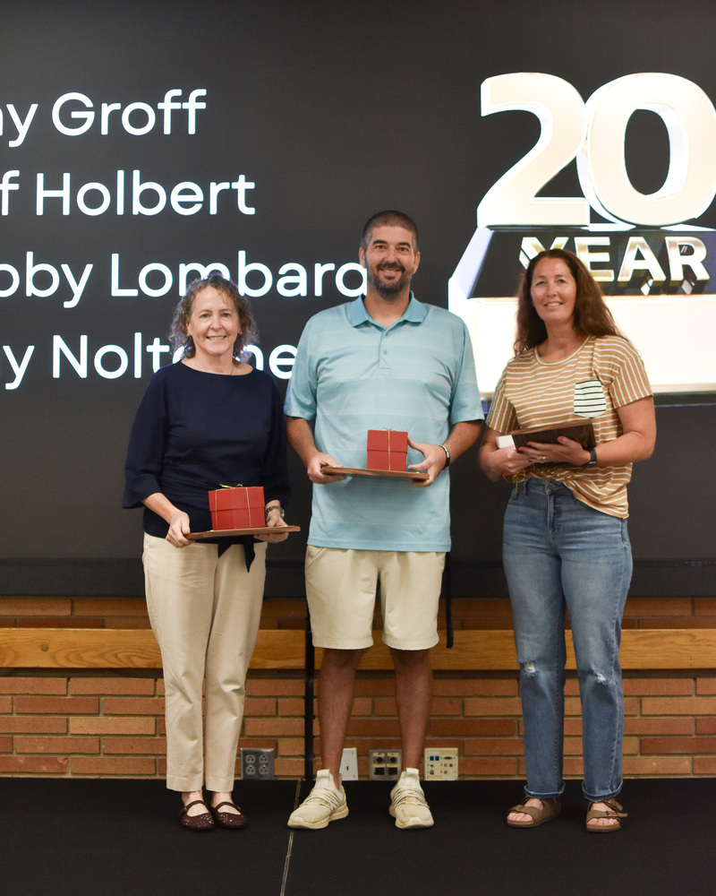 3 staff members stand holding their awards for 20 years of service.