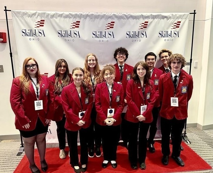 A group of students, male and female, are dressed in red jackets and black pants. in front of the SkillsUsa Ohio backdrop which is white with the SkillsUsa logo. 
