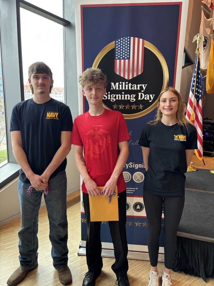 3 students pose in front of a Military Signing Day banner. 