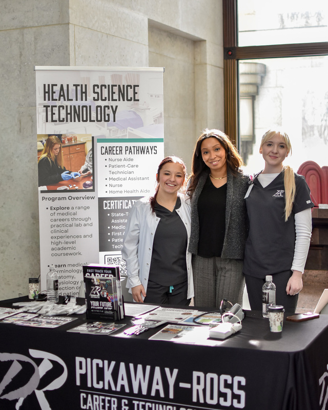 3 nurses stand behind a table. 