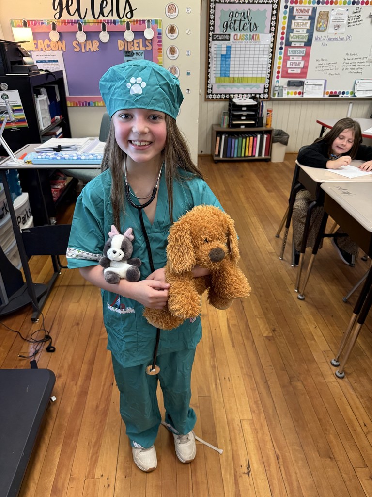 Female student  standing in front of a classroom holding a stuffed animal dog dressed in career day clothes for Red Ribbon Week as a veterinarian.