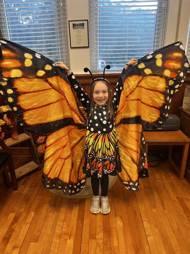 Image of student standing in front office holding a gift bag dressed as a butterfly