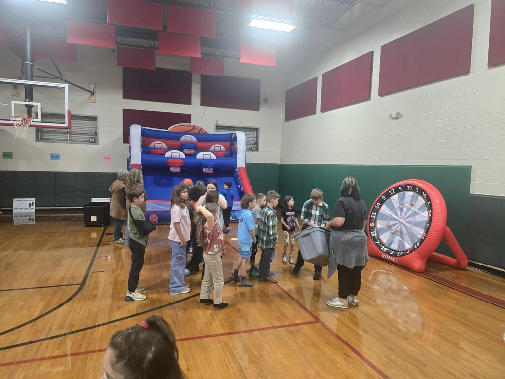 Group of kids standing in a row in a school gym throwing darts at an inflatable dartboard