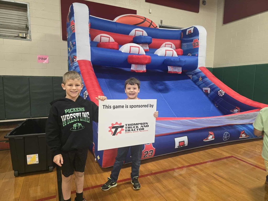 Two kids holding a sign in a school gym holding a sponsorship sign for an inflatable basketball game