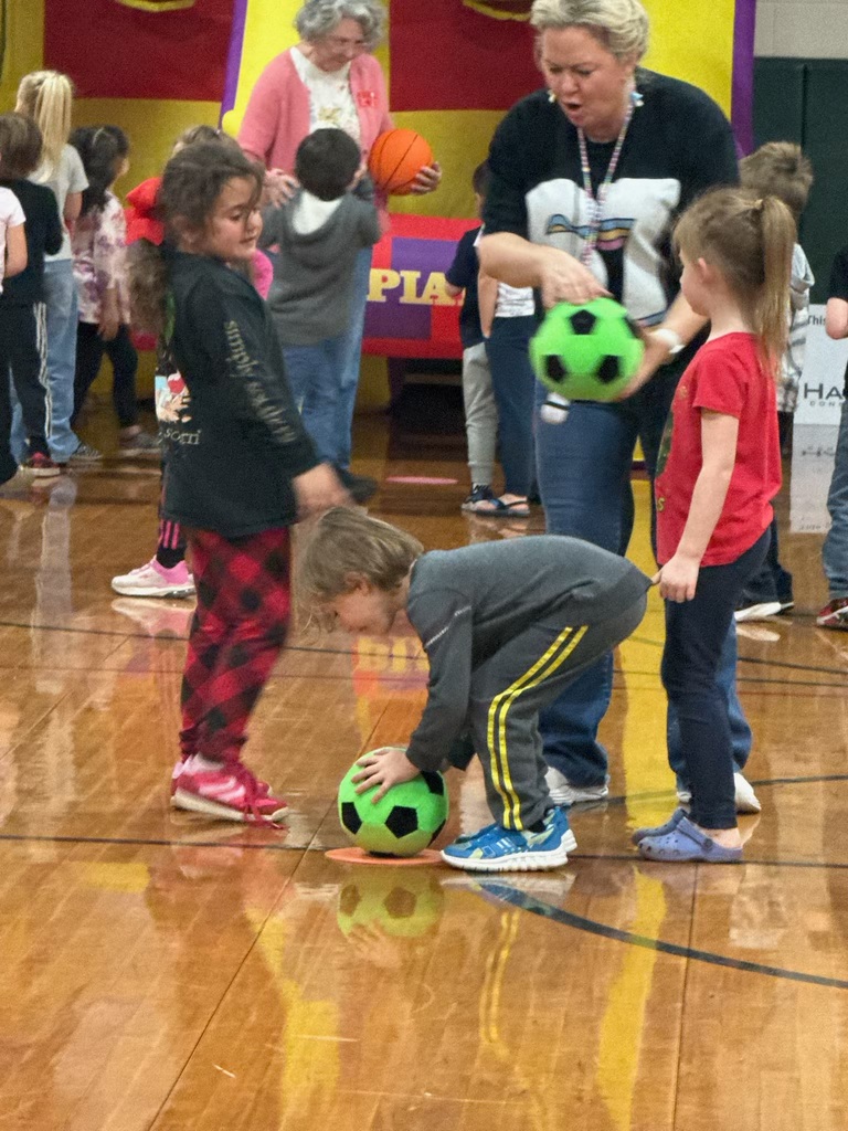 Group of kids and two adults in a school gym playing with green and black soccer balls