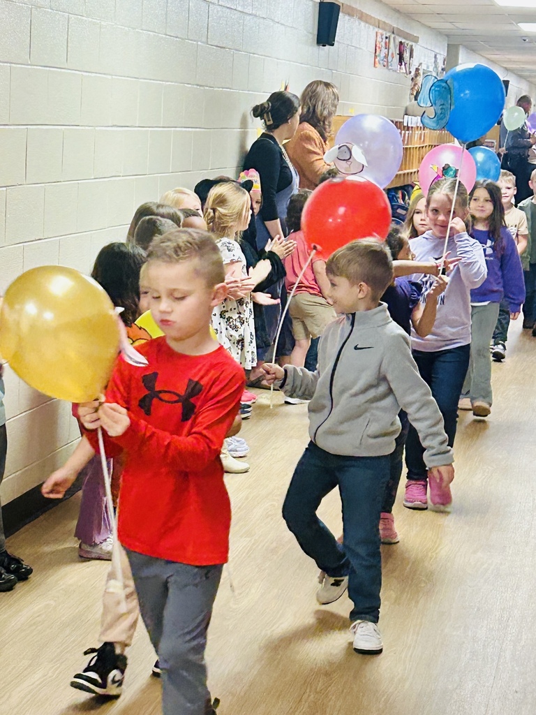 Group of kids walking in a school hallway holding balloons on sticks 